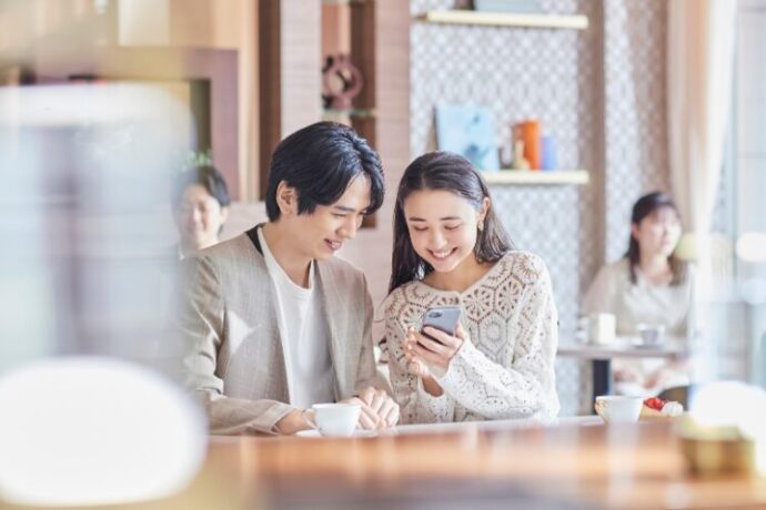 一緒にスマホを見ながら談笑する夫婦_アニヴェルセル