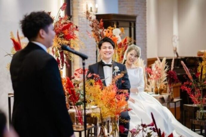 挨拶をする主賓の後ろ姿と微笑む新郎新婦